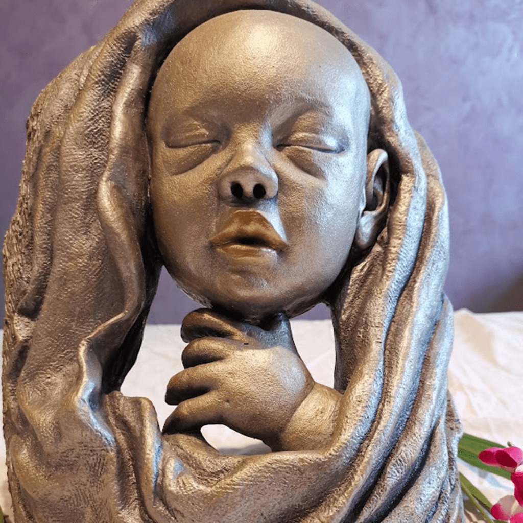Sculpture en argile cuite patinée argent et or, représentant un bébé sorti du bain, une œuvre artisanale pleine de tendresse et de sérénité.